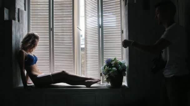 Young blonde model in the blue underwear posing for photographer sitting at the window during fashion photo session — Stock Video