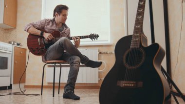 Genç adam müzisyen müzik gitar oluşturur ve mutfak, diğer enstrüman ön planda oynar,