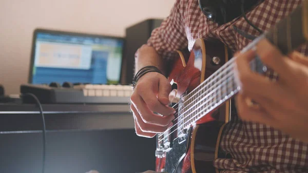 Молодий музикант пише і записує музику, граючи на гітарі за допомогою комп'ютера і клавіатури — стокове фото