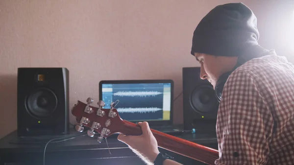 Joven músico masculino compone y graba banda sonora tocando la guitarra usando ordenador, auriculares y teclado —  Fotos de Stock