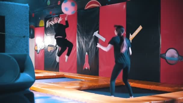 Две симпатичные девушки в акробатическом зале на батуте играют в мяч, замедленная съемка — стоковое видео