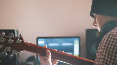 Genç erkek müzisyen oluşturur ve bilgisayar, kulaklık ve klavye kullanarak gitar çalmak soundtrack kayıtları