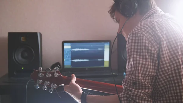 Joven músico masculino compone y graba la banda sonora tocando la guitarra usando la computadora —  Fotos de Stock