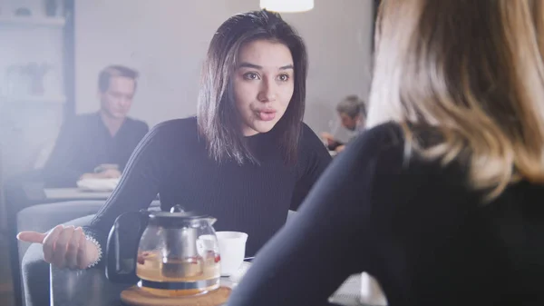 Svart haired ung kvinna med svart hår dricker kaffe och pratar med flickvän i caféet — Stockfoto