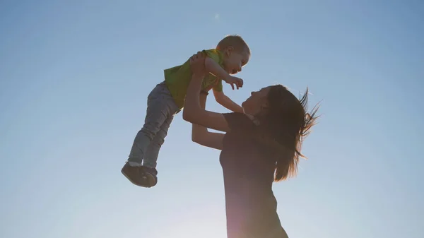 Мати грає з маленькою дитиною на заході сонця кидає сина — стокове фото