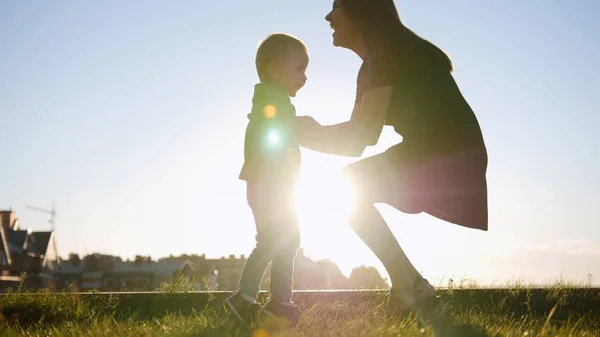 Moeder speelt met zoontje bij zonsondergang - gooit het kind — Stockfoto