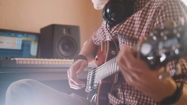 Молодий музикант пише і записує саундтрек, граючи на гітарі за допомогою комп'ютера і клавіатури — стокове фото