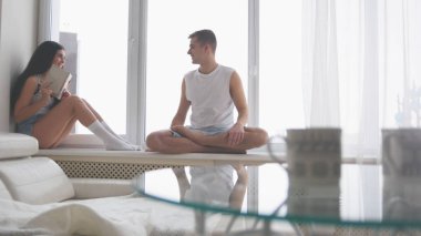 Pencere kenarında, bir kitap okuma ve gülen kız oturan genç mutlu çift adam onu gıdıklıyor