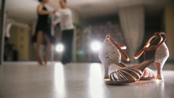 Homem e mulher desfocados dançando dança latina em trajes no estúdio, sapatos de salão em primeiro plano, câmera lenta — Vídeo de Stock