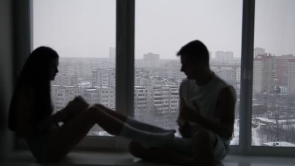 Sziluettjét, egy fiatal, boldog pár ül az ablak előtt havas téli nap — Stock videók
