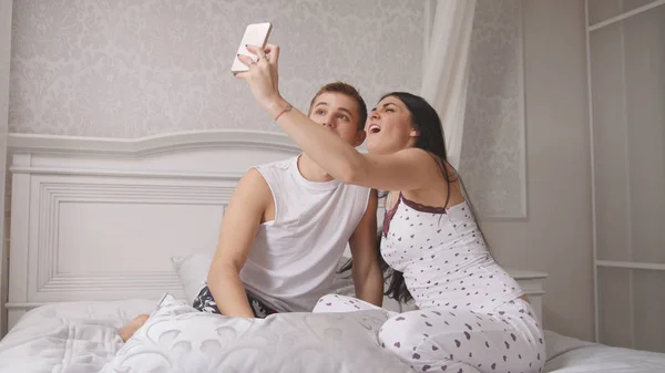 Szczęśliwy wesoły miłości para co selfie w łóżku, młody atrakcyjny facet i dziewczyna siedzi w piżamie — Zdjęcie stockowe