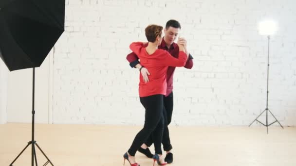 Frau mittleren Alters und junger Mann in rotem Hemd tanzen Kizomba im Studio — Stockvideo