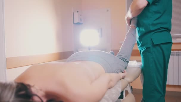 Мануальний терапевт масажує молоду жінку, що лежить на масажному столі, розтягуючи ноги — стокове відео