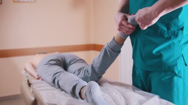 Chiropratico massaggiare una donna sdraiata su un tavolo da massaggio, allungando e flettendo i piedi e il ginocchio, primo piano delle gambe — Video Stock