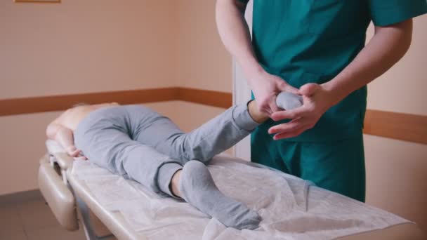Εγχειρίδιο θεραπευτής μασάζ μια νεαρή γυναίκα που βρίσκεται σε ένα τραπέζι μασάζ, τέντωμα και λύγισμα της πόδια, γόνατα και δάχτυλα — Αρχείο Βίντεο