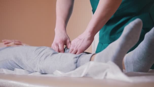 Хиропрактик массирует молодую женщину, лежащую на массажном столе, растягивая колени — стоковое видео