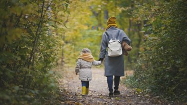 Neşeli küçük kızı ile onu anne ve Teddy Bear sonbahar park, dikiz yürür