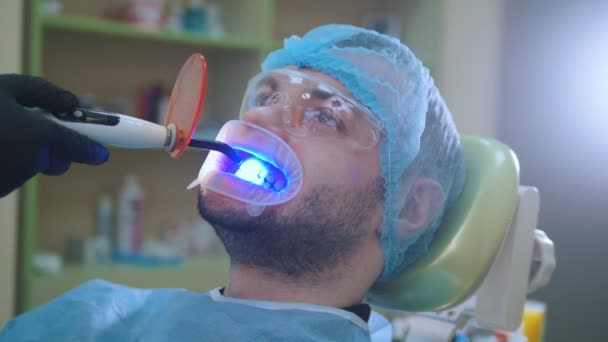 Doctor and patient with retractor in the dental office, cleaning with ultraviolet light and orange protective screen — Stock Video