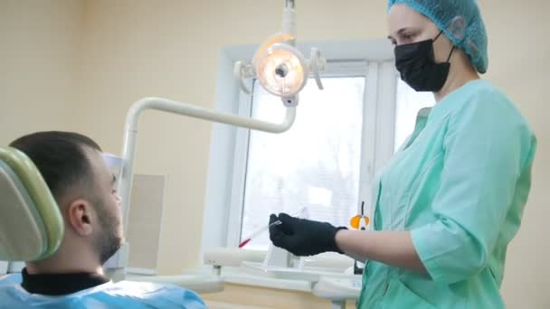 Médico estomatólogo y paciente en el consultorio dental, preparación para el tratamiento, el paciente con gafas protectoras — Vídeos de Stock