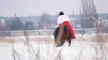 Kış aylarında karla kaplı alan üzerinden bir at üzerinde yürüyen bir Kırmızı elbiseli çekici genç esmer