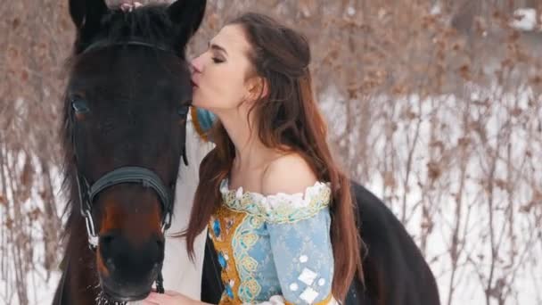 Atractiva morena de pelo largo en un vestido y su caballo en invierno, besándose y sonriendo — Vídeo de stock