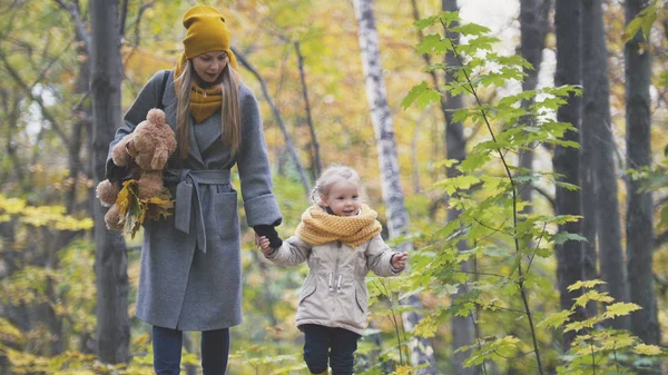 Маленькая дочь с матерью и медвежонком Тедди гуляет в осеннем парке — стоковое фото