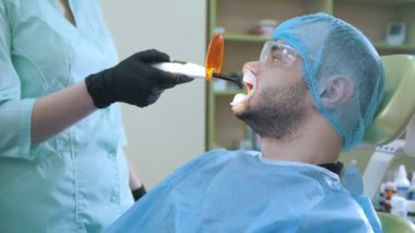 Doktor ve hasta diş ofiste, bağımsız dolguların turuncu koruyucu ekranlı polimerizasyonu