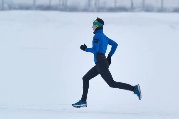 Ung manlig idrotts man kör snabbt på vintern genom snön — Stockfoto