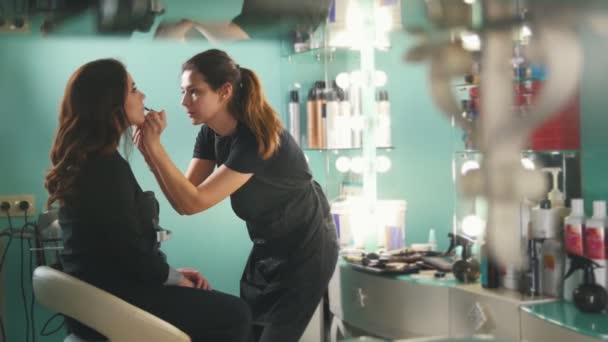 Maquiagem artista no salão de beleza faz para menina atraente bela maquiagem, cabeleireiro faz penteado, close-up — Vídeo de Stock