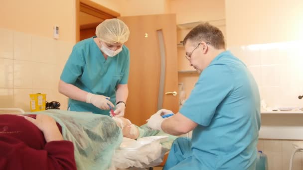 Cirugía médica para la rodilla: el médico y la enfermera drenan el líquido de la rodilla de los pacientes con una jeringa, se acercan — Vídeo de stock