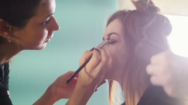 Artista de maquillaje y peluquero trabajando con el cliente en el salón de belleza, aplicando sombra de ojos — Vídeo de stock