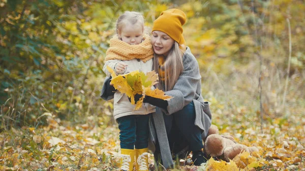 Blond liten dotter med hennes mamma promenader i höst park - har roligt och samla löv, närbild — Stockfoto