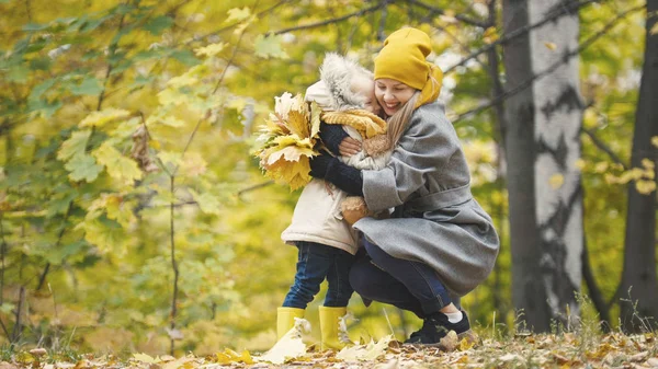 Malá dcera s její máma hraje s žluté listí v podzimním parku — Stock fotografie