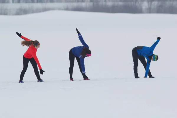 Grupp av idrottare gör träningen i vinter fält — Stockfoto