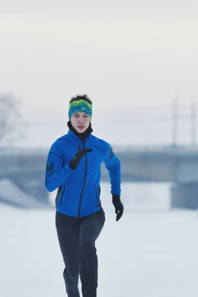 Ung manlig idrottsman som kör på vintern i snön — Stockfoto