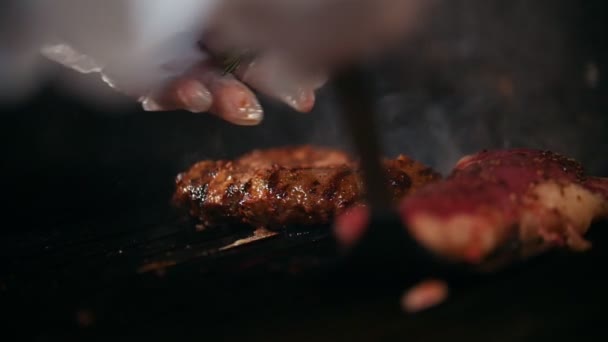 Близько двох шматків м'яса різного ступеня готовності лежать на грилі, шеф-кухар перевертає один з них — стокове відео