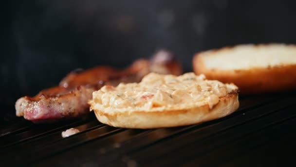 Повар готовит бургер, жарит булочку на гриле, кладет помидоры — стоковое видео