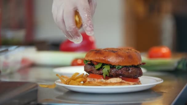 Chef serves a burger by adding potato chips on a plate — Stock Video