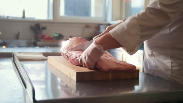 Macellaio taglio grande pezzo di carne fresca cruda sdraiato su una tavola di legno in una cucina commerciale — Video Stock