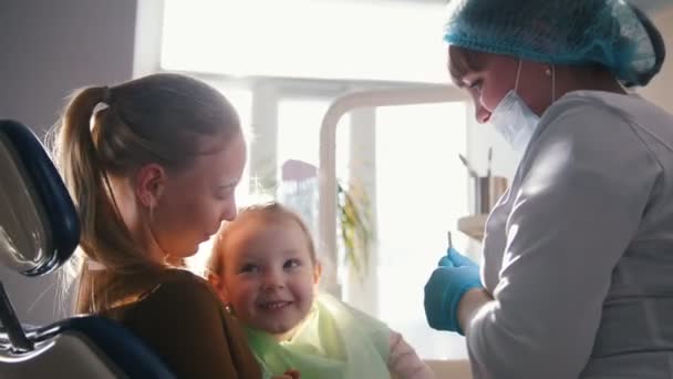 Niño pequeño con mamá en silla de estomatología - niña sonríe — Vídeos de Stock