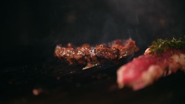 Close up of two slices of meat of varying degrees of readiness lie on the grill, chef turning one of them — Stock Video