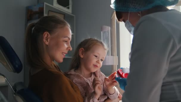 Meisje, haar moeder en de tandarts in de tandheelkundige kantoor, de stomatologist adviseren met een speciale speelgoed — Stockvideo