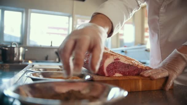 Macellaio aggiunta di spezie in un grande pezzo di carne fresca cruda sdraiato su una tavola di legno in una cucina commerciale, slow motion — Video Stock