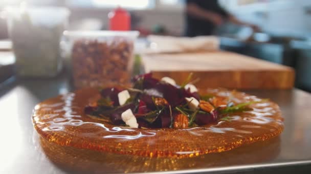 Шеф-повар обслуживает салат, помещая компоненты на тарелку и добавляя соус, свежие овощи на переднем плане — стоковое видео