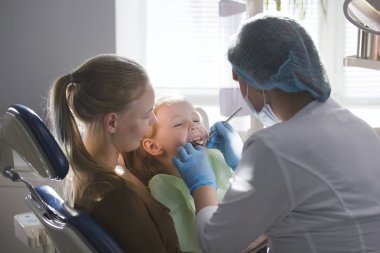 Kız, annesi ve diş hekimi diş office, incelenmesi ve danışmanlık stomatologist, kızı oynamaya ve şikayet