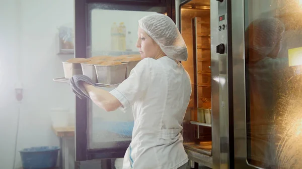 Kvinnliga bakar på kommersiella kök - drar bröd från ugnen — Stockfoto
