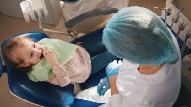 Petite fille mignonne dans le bureau des dentistes ne veut pas être traitée, souriant, résistant et fermant sa bouche avec ses mains — Video