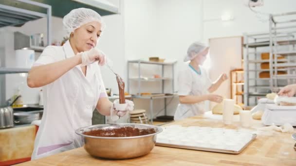 Женщина-пекарь смешивает шоколадный крем в металлической миске и делает торты — стоковое видео