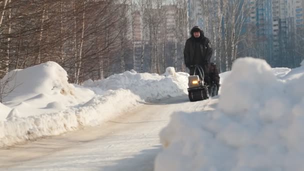 Человек едет на снегоходе с прицепом и пассажиром по зимней дороге — стоковое видео