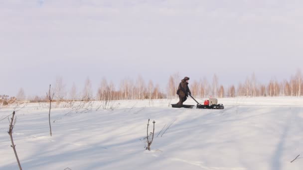 Man in de winter kleding lopen en rijden op mini sneeuwscooter op diepe sneeuwlaag op het gebied — Stockvideo